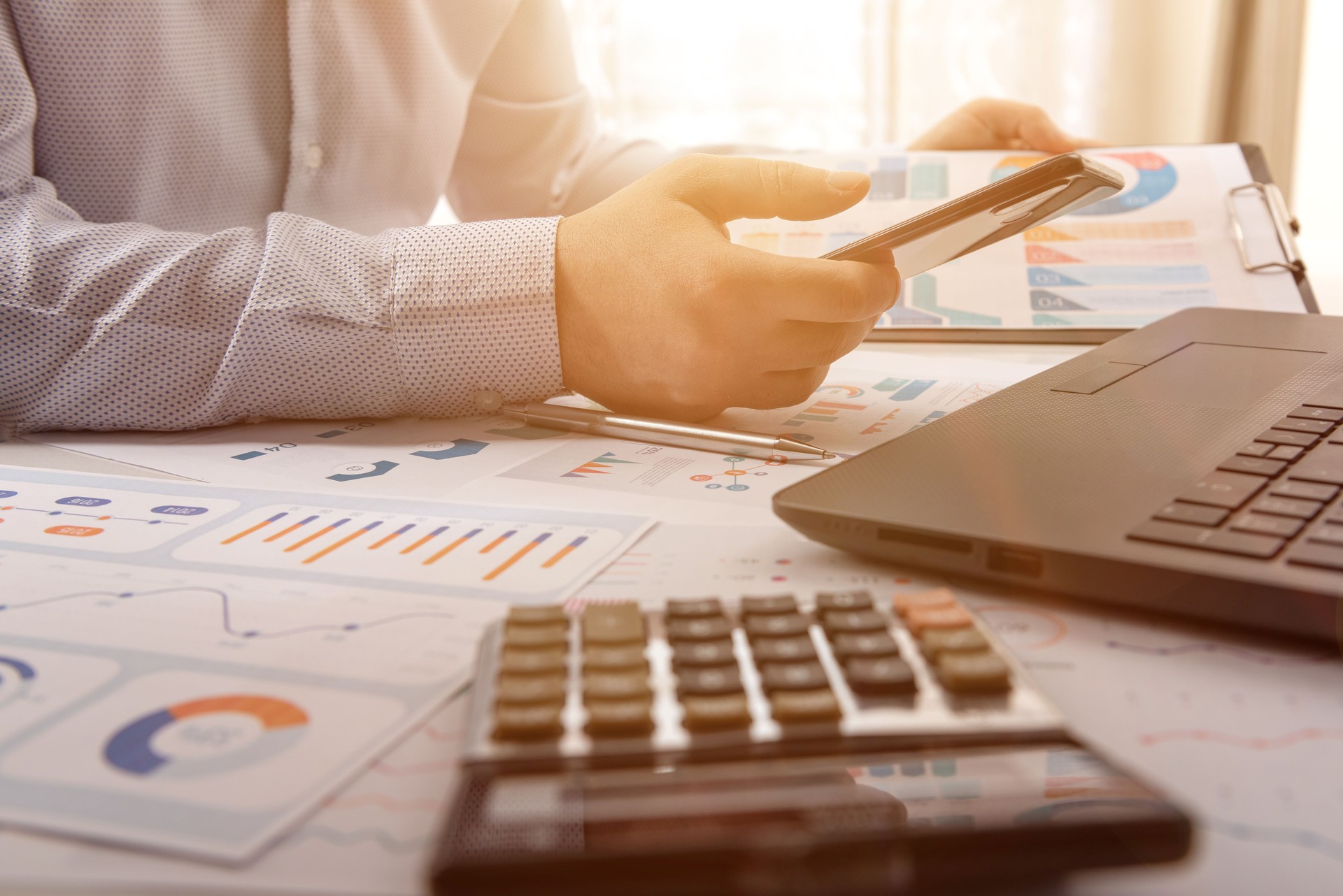 Businessman looking at financial data with his smart phone at his office desk. Business accounting concept.